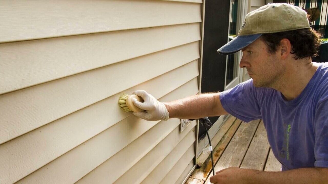 man washing vinyl siding by hand with brush