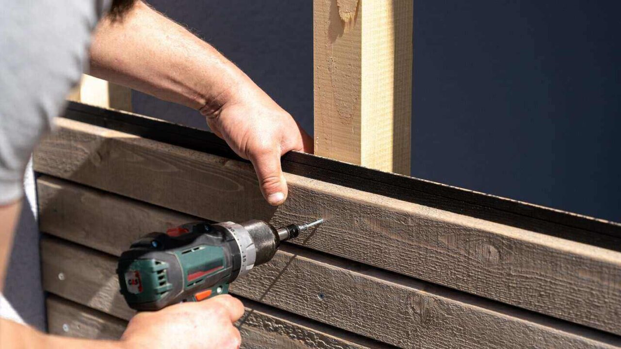 construction worker applies wooden siding to a garage and drills screws