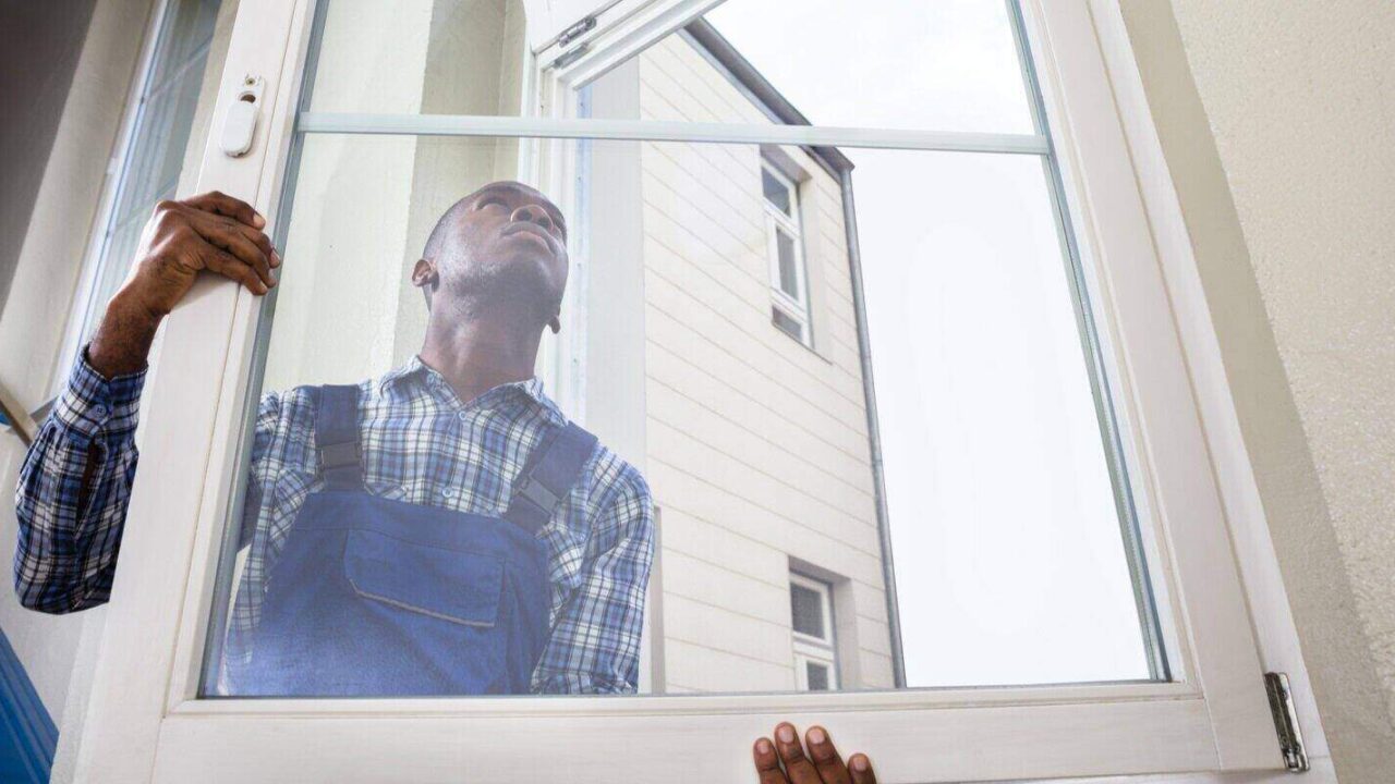 african handyman in uniform installing window