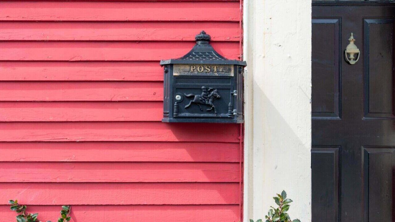 exterior wall of a colorful red wooden clapboard siding house with a black metal mailbox