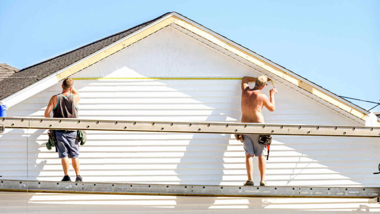 contractor working on exterior structure measuring siding for installation