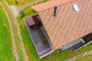 Private house and its territory top view. Roof of cottage and its terrace. Stone path next to country house. Concept - sale of roofing materials. Roof of house is covered with flexible tiles.